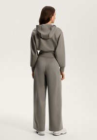 Felpa grigia corta con cappuccio, abbinata a pantaloni grigi a gamba larga. Tessuto morbido, cintura elastica e polsini a costine. Design semplice, senza fantasie.