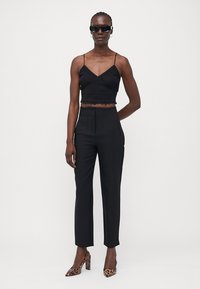 Svart strikket crop-top med bølget kant, sammen med høyt liv svarte bukser. Komplimentert av leopardmønstrede hæler og solbriller.