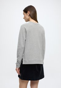 Szürke pulóver kerek nyakkivágással és bordázott mandzsettákkal, fekete kordbársony szoknyával párosítva, oldalán sliccel és texturált anyaggal.