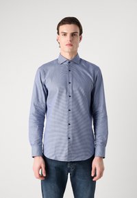 Camicia a quadri blu con maniche lunghe, colletto alla coreana e bottoni scuri, abbinata a jeans in denim scuro.