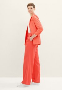 Coral blazer and wide-leg trousers in lightweight fabric. Features a notch lapel and front pockets. Paired with white sneakers.