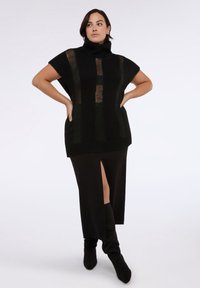 Top de punto negro con cuello alto y mangas cortas, que presenta rayas verticales translúcidas; combinado con una falda larga negra y botas hasta la rodilla.