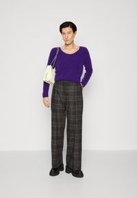 Pulover tricotat mov, pantaloni cu talie înaltă din material cu carouri în nuanțe de gri, asortați cu o geantă de mână de culoare deschisă și cizme masive negre.