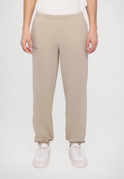 Beige sweatpants med elastisk talje og manchetter, der har et minimalistisk design og subtil typografi detalje på venstre lår.