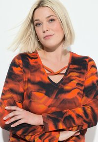 V-neck long-sleeve top featuring an abstract pattern of red, orange, and black colors with crisscross detailing near the neckline.