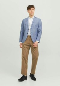 Błękitna lniana marynarka, biała koszula na guziki, beżowe spodnie i czarne buty. Marynarka ma dwa guziki i naszyte kieszenie.