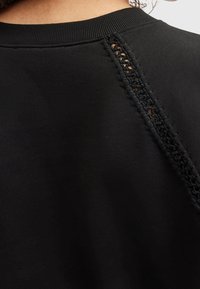 Czarna bluza z teksturowanym detalem na szydełkowanym szwie. Miękki materiał, klasyczny okrągły dekolt i gładka powierzchnia.