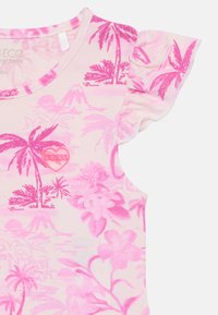 Pink short-sleeve top with floral and palm tree pattern. Features ruffled sleeves and a heart-shaped logo in the center. Cotton blend material.