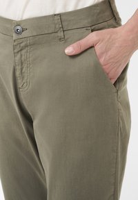 Pantaloni verde oliva realizzati in tessuto morbido, con chiusura a bottone, tasche laterali e una superficie liscia. Vista ravvicinata della vita e dell'area delle tasche.