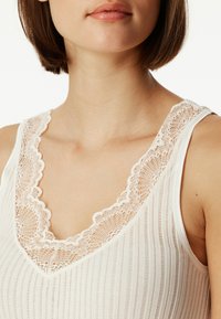 White tank top with vertical stripes, lace trim around the neckline, smooth texture, and wide shoulder straps. Subtle scalloped edges.