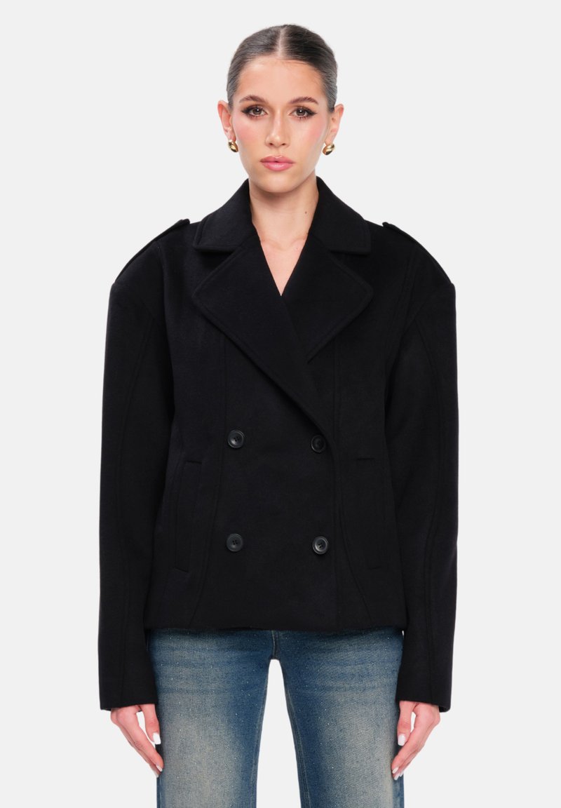 Sort dobbeltradet uld peacoat med brede klapper, sidelommer og store skuldre, båret over blå jeans.