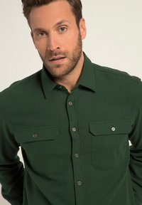 Camisa verde de botones, hecha de una tela suave, con dos bolsillos en el pecho, detalles de botones plateados y un diseño de cuello clásico.
