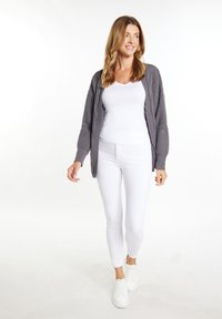 Cardigan grigio lavorato a maglia su una maglietta bianca aderente, abbinato a jeans skinny bianchi e sneakers bianche. Texture liscia, vestibilità rilassata e design a strati.