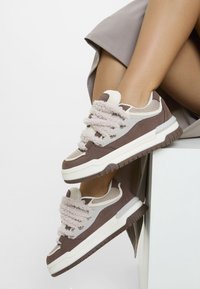 Sneakers med en kombination av brun mocka och mesh, ljusgrå accenter, fluffiga texturerade snören och en tjock vit mellansula.