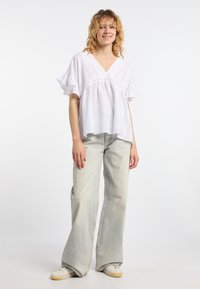 Hvid, let tekstureret, kortærmet bluse med V-udskæring og samlet talje. Parret med lysegrå klæbrige jeans og hvide sneakers.