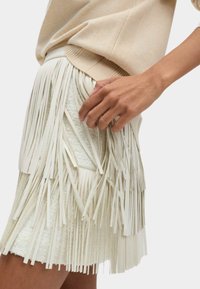 Jupe à franges de couleur crème clair avec un tissu texturé et de longues franges fines le long de l'ourlet, associée à un pull beige.