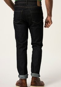 Mörkblå denimjeans med en avsmalnande passform, med uppvikta fållar, orange sömmar och två bakfickor. Bruna läderankelboots synliga.