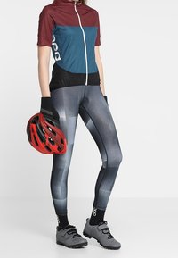 Punainen ja musta pyöräilykypärä, sininen ja viininpunainen lyhythihainen paita, kuvioidut harmaat legginssit, harmaat pyöräilykengät ja mustat rannekäärmeiset käsineet.