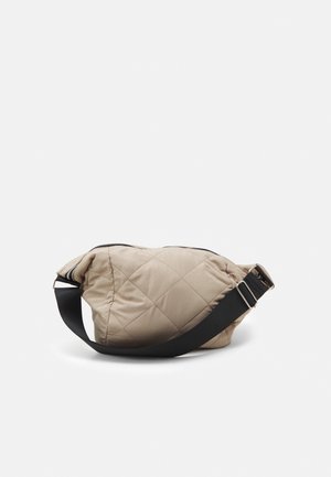 Sac à épaule beige matelassé avec fermeture éclair, une sangle noire réglable et une forme arrondie. Texture lisse avec des détails en motif de losange.