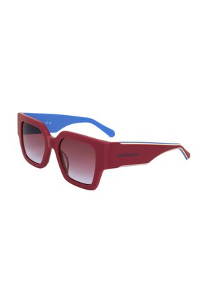 Occhiali da sole con montatura quadrata rossa, aste interne blu e lenti scure sfumate, logo Calvin Klein Jeans sul lato.