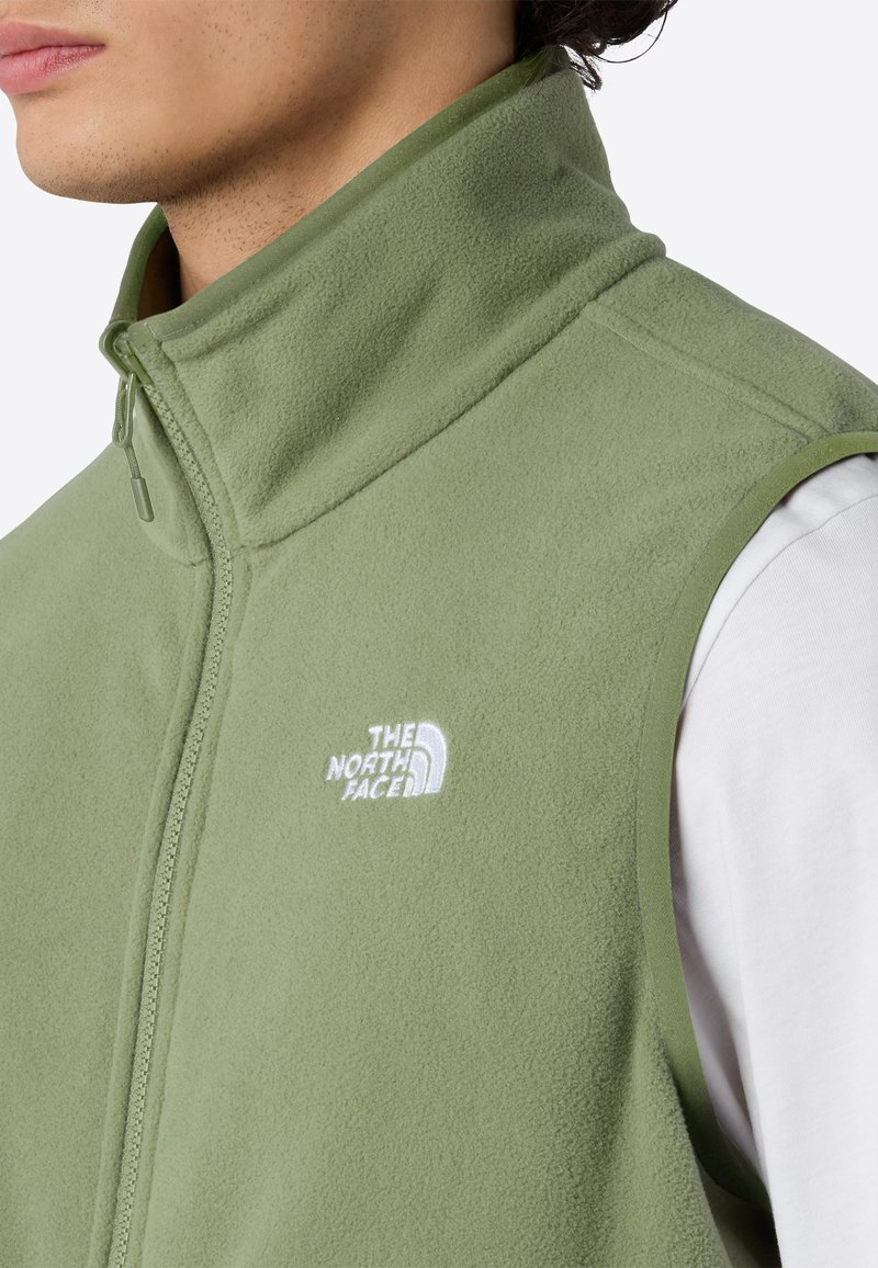 Grüne Fleeceweste mit hohem Kragen, Reißverschluss und Logo auf der linken Brust. Weiche Textur und einfarbig ohne Muster oder Akzente.