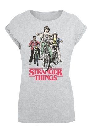Camiseta gris de manga corta con un estampado gráfico de tres personajes en bicicletas, con el texto "STRANGER THINGS" en rojo negrita.