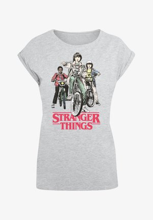 Camiseta gris de manga corta con un estampado gráfico de tres personajes en bicicletas, con el texto "STRANGER THINGS" en rojo negrita.