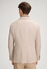 Beżowa, dopasowana marynarka o zdefiniowanym kształcie, miękkiej fakturze i subtelnym wzorze. Posiada klapy z wycięciem oraz brązowe guziki jako akcenty.