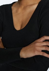Schwarzes, geripptes Langarmoberteil mit tiefem V-Ausschnitt und strukturiertem Muster. Der Stoff wirkt weich und hat eine taillierte Silhouette.