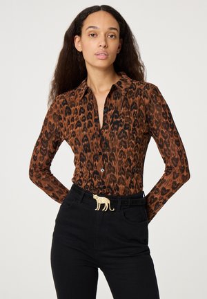 Bruine langarm blouse met luipaardprint, voorzien van een spitse kraag en een knoopsluiting aan de voorkant, gecombineerd met zwarte jeans met hoge taille en een gouden riemgesp met dierenmotief.