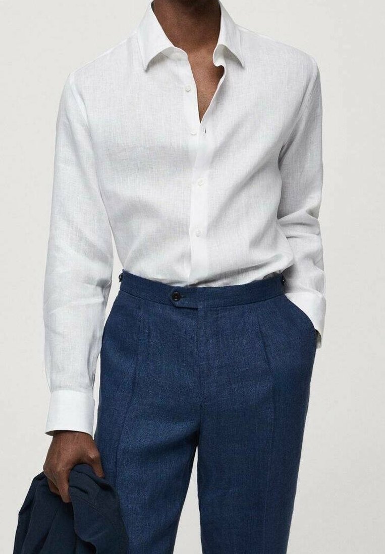 Witte linnen shirt met een button-down kraag, gecombineerd met donkerblauwe gestructureerde broeken met voorplooien en dubbele knopen.