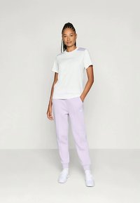 T-shirt blanche à manches courtes avec une accent lavande sur l'épaule, associée à un pantalon de survêtement lavande, le tout fabriqué dans un tissu doux et respirant.