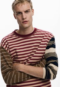 Striped long-sleeve shirt featuring varying widths of burgundy, beige, and brown stripes, with a navy blue sleeve and soft fabric texture.