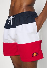 Shorts de bain pour homme en bleu marine, blanc et rouge avec une taille élastique, un cordon de serrage, des poches latérales et un détail de logo brodé.