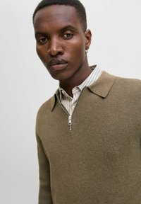 Oliivroheline lukuga sviiter, millel on tekstuuriga viimistlus ja terav krae. All on nähtav valge ja heledates hallides triipudega särk.