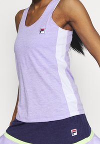 Fialový sportovní top s kulatým výstřihem, kontrastními bílými bočními panely a malým logem FILA na hrudi. Hladká, lehká látka.