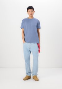 Ανοιχτό μπλε υφασμάτινο μπλουζάκι, χαλαρές μπλε τζιν παντελόνες, καφέ αθλητικά παπούτσια και μια κόκκινη μαντίλα στην τσέπη. Απλή, μοντέρνα εφαρμογή, ελάχιστες λεπτομέρειες.