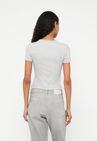 Grey short-sleeve t-shirt with a fitted design, made of cotton blend material. Worn with light grey high-waisted jeans, showcasing back details.