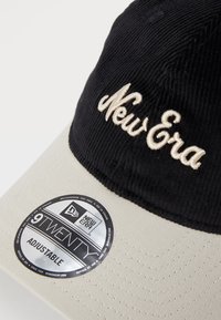Sort fløjlskappe med justerbar beige skygge, med broderet "New Era" logo i creme og et rundt mærke med teksten "9TWENTY."