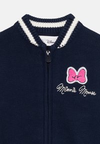 Námornícky pletený sveter na zips s bielym pruhovaným golierom a vyšitou ružovou mašľou a textom "Minnie Mouse" na ľavej strane hrudi.
