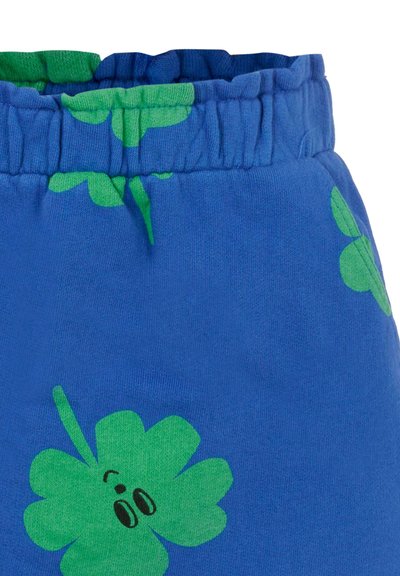 Blå bomullsshorts med ett grönt klövermönster, med elastisk midja och mjuk textur. Designen inkluderar lekfulla ögon på klövern.