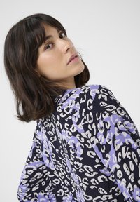 Blouse à manches longues en bleu marine avec un imprimé léopard violet et blanc audacieux, présentant une coupe décontractée et une texture de tissu douce.