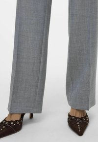 Pantaloni grigi su misura in tessuto strutturato, abbinati a scarpe con tacco marroni scure con bordi scallop e occhielli decorativi.