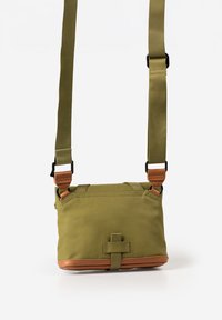 Small olive green crossbody bag with adjustable straps, leather trim at the bottom, and a front loop detail.