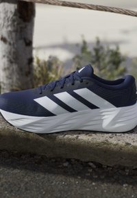 Navy blue athletic shoe with white stripes and thick white sole resting on a concrete ledge outdoors.