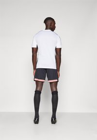 Urheiluasu, joka sisältää valkoisen lyhythihaisen paidan, mustat shortsit vaaleanpunaisilla yksityiskohdilla ja mustat polvipituiset sukat. Suorastaan sileä rakenne, istuva muotoilu.