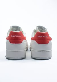 Sneakers bianchi in pelle con una linguetta rossa sul tallone, caratterizzati dalla scritta "Sergio Tacchini" stampata in bianco, superfici testurizzate e una suola grigia imbottita.