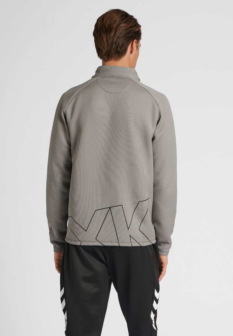 Grauer sportlicher Pullover mit langen Ärmeln und hohem Kragen, der auf der Rückseite ein geometrisches schwarzes Logo und einen strukturierten Stoff aufweist.