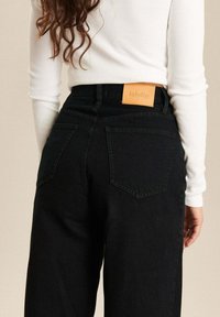 Zwarte high-waisted jeans van denim, met een leren label aan de achterkant en twee achterzakken met een klassiek ontwerp.
