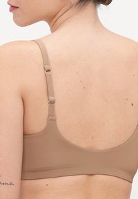 Light brown bra with adjustable straps, smooth texture, and a simple design. Features minimal stitching and a back clip closure.